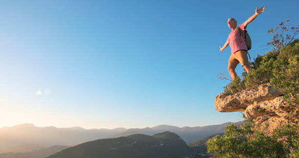 istock Mature man stands on cliff edge at sunset 2184390246