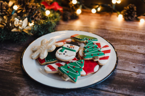 istock Christmas cookies on sheet or plate with golden lights on rustic table. Baking traditional snowman, tree, star cookies and santa hat 2184391134