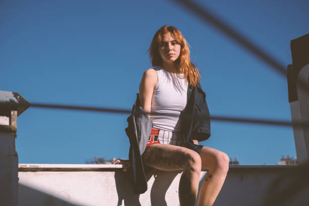 A gorgeous young woman posing on a rooftop under sunlight.