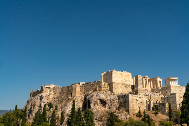 A serene view of Athens showcasing the weathered stone structures of a majestic Greek temple silhouetted against a clear azure sky.