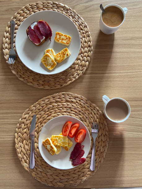 istock Cozy breakfast setting features plates with cheese, tomatoes, and cured meat, complemented by cups of coffee. Woven placemats and wooden table provide a warm, inviting ambiance 2184410969