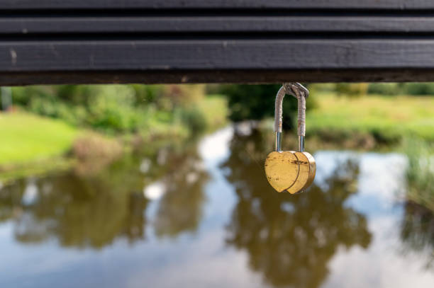 A golden heart lock dangles from a bridge with a serene pond in the background.