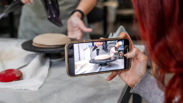 istock In an art studio with an environment adorned with artistic paintings in the background, a beautiful middle-aged woman artist is shaping clay at a table, while a young woman next to her is taking a photo with her phone 2184423898