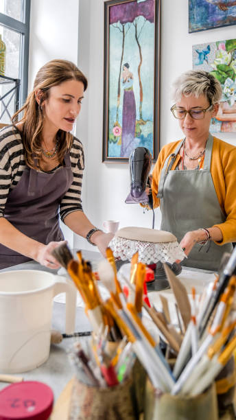 istock In an art studio with an environment adorned with artistic paintings in the background, two beautiful middle-aged artist friends are drying a clay-shaped plate with a hairdryer at a table 2184424031