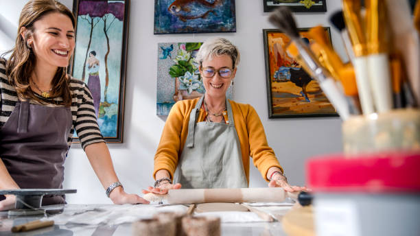 istock In an art studio with an environment adorned with artistic paintings in the background, two beautiful middle-aged woman artist is shaping clay with a rolling pin at a table 2184424080