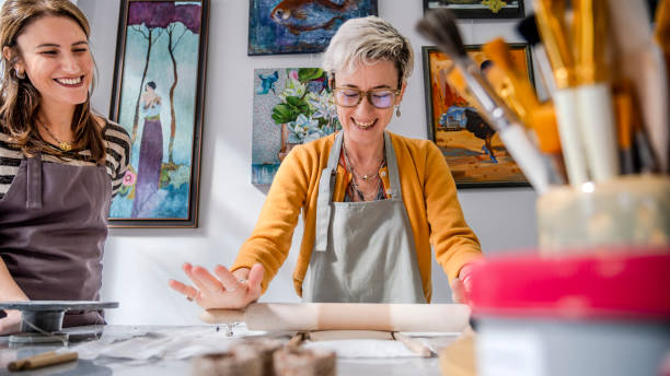 istock In an art studio with an environment adorned with artistic paintings in the background, two beautiful middle-aged woman artist is shaping clay with a rolling pin at a table 2184424088