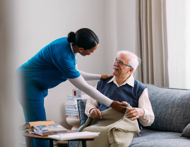 istock Caregiver Assisting Smiling Elderly Man with Blanket at Home 2184430175