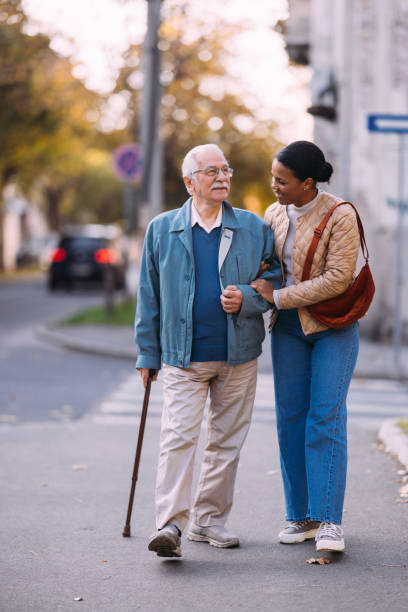 istock Elderly Man Assisted by Young Woman on a Pleasant Walk 2184430178