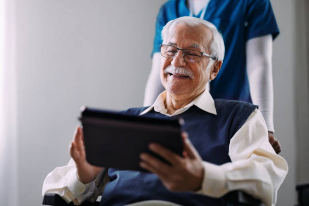 istock Smiling Elderly Man Using Digital Tablet at Home with Caregiver 2184430255