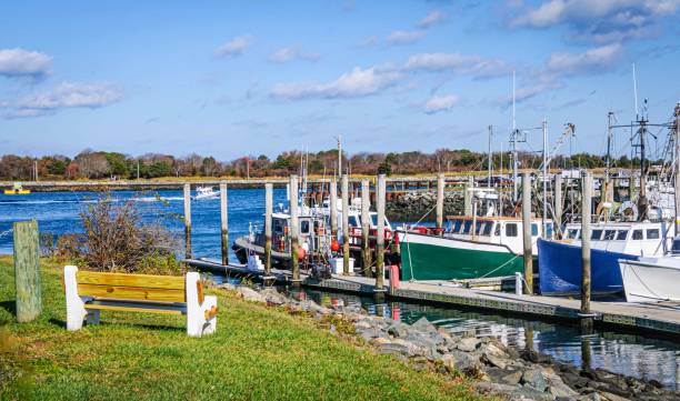 A bench at the Sandwich, Massachusetts marina overlooks a dock with commercial fishing blats and the waters of the Cape Cod Canal on a November afternoon.