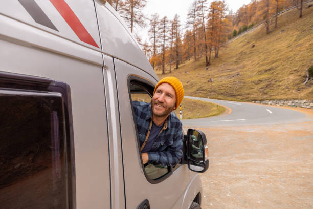 istock Man Looking Out from Camper Van on Scenic Road 2184442776