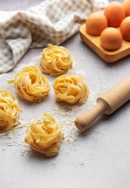 istock Tagliatelle nests with flour, eggs and rolling pin composing a beautiful food background 2184454520