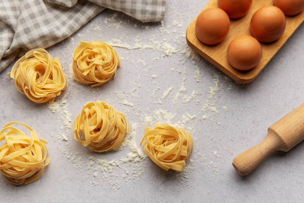 istock Tagliatelle nests with flour, eggs and rolling pin composing a beautiful food background 2184454529