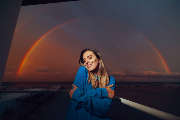 Happy Woman Hugging Herself Under a beautiful Rainbow