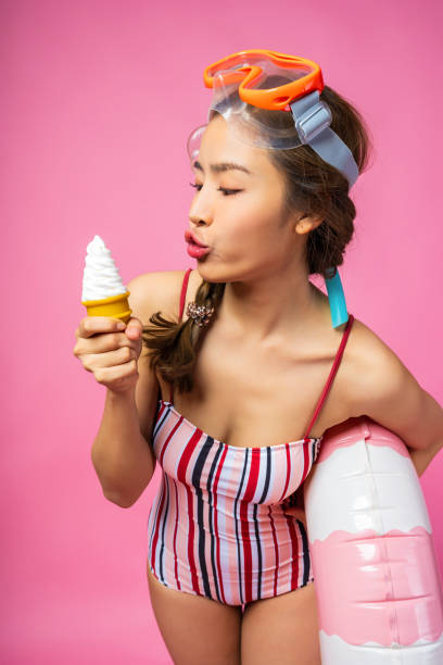 istock A young woman enjoying ice cream while playfully posing with a float in a vibrant pink setting. 2184471202