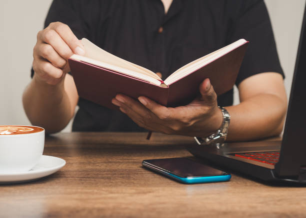 istock Person reading book with coffee and smartphone on desk, relaxation and learning concept 2184473168