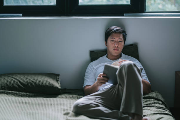 istock Asian Chinese man eating and reading book on bed weekend day time 2184476667