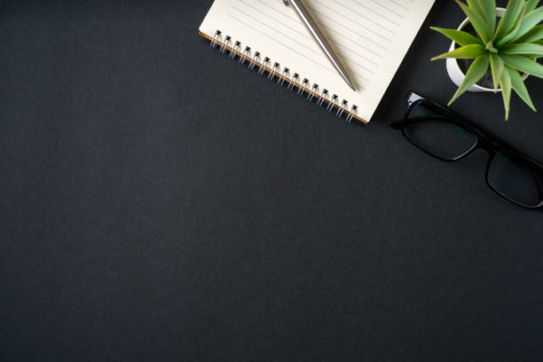 istock Top view of notebook, glasses and ballpoint pen on dark grey background 2184487428