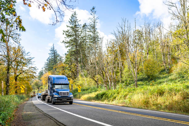 istock Bonnet blue big rig long haul semi truck transporting fastened cargo on flat bed semi trailer driving on the autumn forest road 2184488513