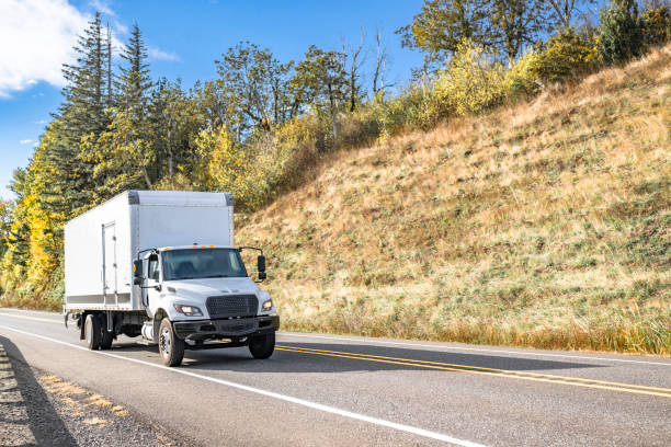 istock Compact white day cab rig semi truck transporting cargo in box trailer running on the narrow road between two hills with autumn trees 2184488766