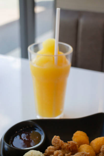 A Japanese lady sitting an outside bar overlooking some scenery while partaking in colorful beverages containing alcohol and fruit juices and working on her laptop
