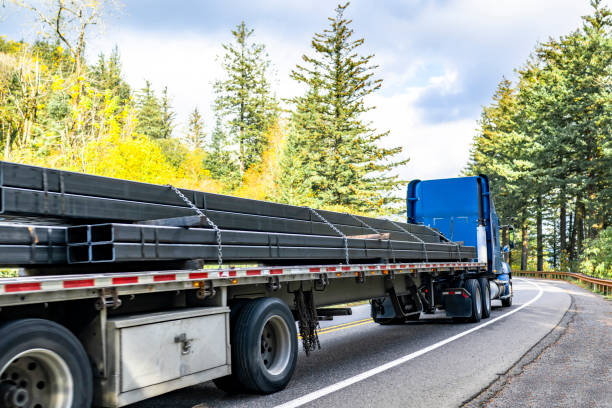 istock High cab blue big rig semi truck tractor transporting fastened by chains metal cargo on flat bed semi trailer running on the winding autumn highway road 2184489133