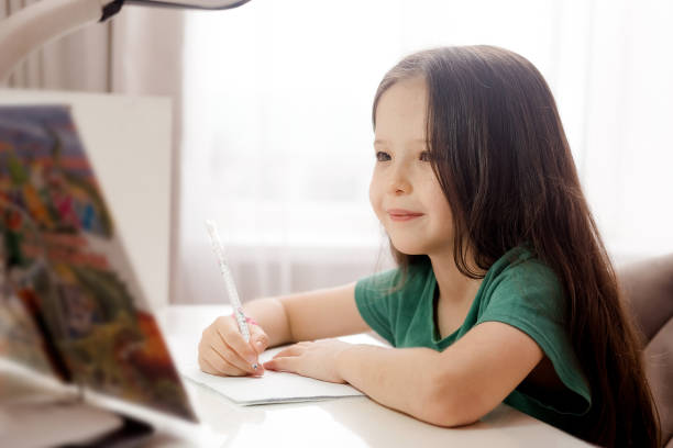 istock A little Caucasian girl is sitting at a table and doing her homework. 2184495342