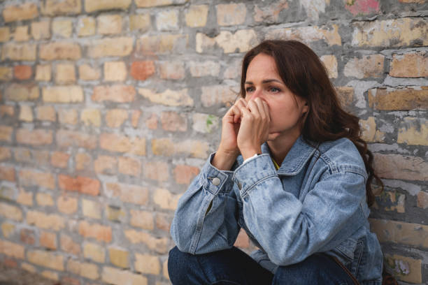 istock Frustrated Caucasian woman sits next to brick wall. 2184495396