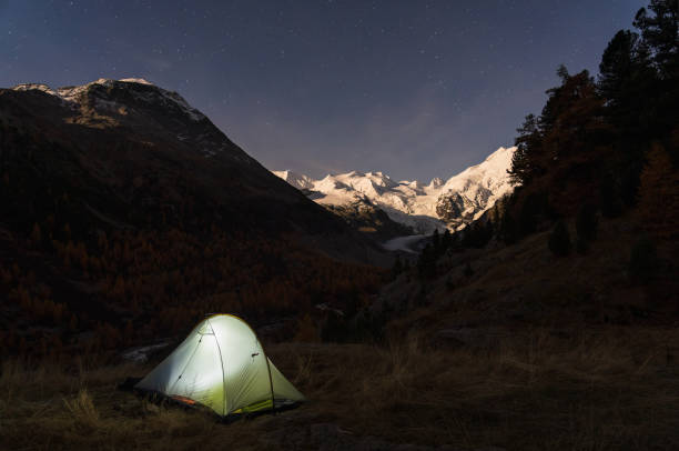 A tent under the night sky in the moonlit Bernina mountain group, Switserland.