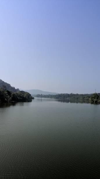 istock Calm river flowing through lush green landscape under clear blue sky. 2184500097
