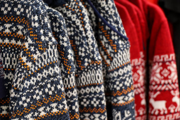 Various knitted turtleneck sweaters and pullovers with norwegian ornament on hanger rack in a clothes store or at a wardrobe, selective focus