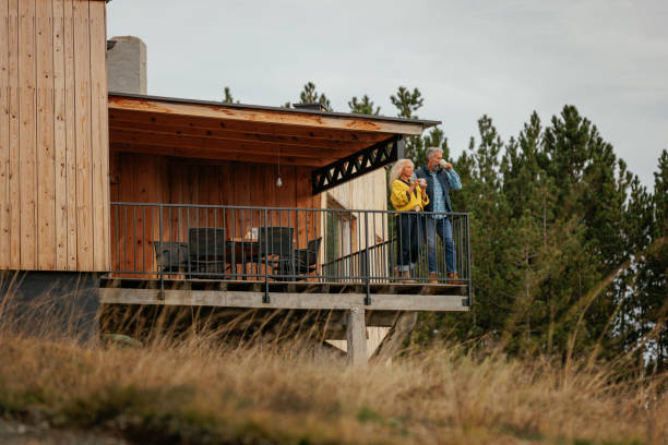 A senior Caucasian couple is enjoying a cup of coffee on their mountain home deck and enjoying the view.