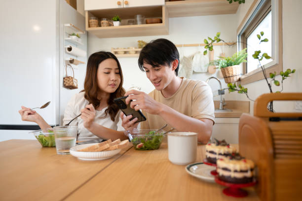 istock Happy young couple using smartphone during lunch in kitchen at home 2184505152
