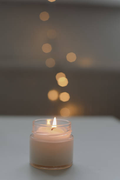 istock Cozy home interior decor, burning candle on table against blurred lights. Handmade scented soy wax candle in a glass. space for text. 2184505232