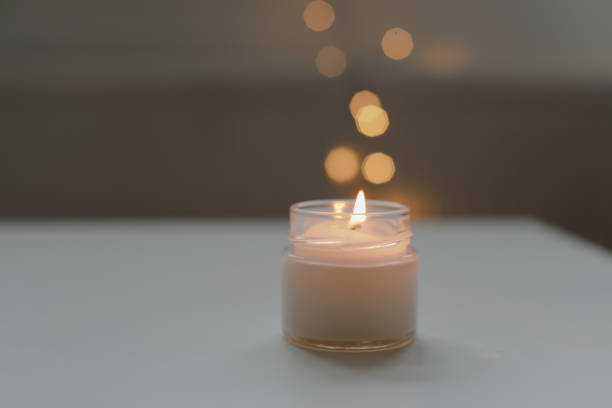 istock Cozy home interior decor, burning candle on table against blurred lights. Handmade scented soy wax candle in a glass. space for text. 2184505408