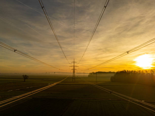 A serene view as the sun descends, casting golden hues over a landscape crisscrossed by towering electrical transmission towers and stretched cables.