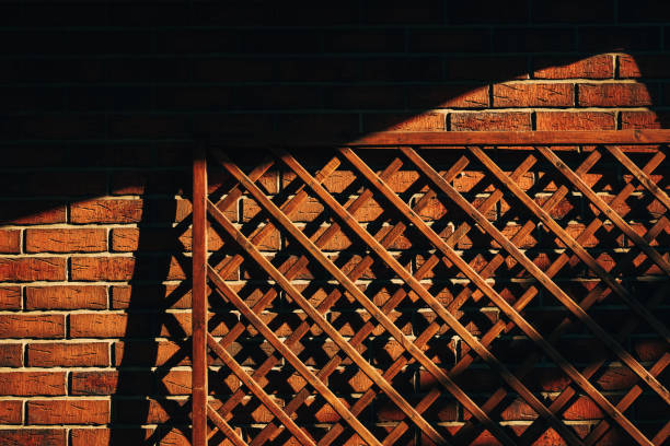 Wooden garden trellis fence panel leaning against the rustic brick wall as background