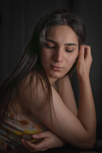 A reflective woman sitting gracefully, illuminated by soft light, creating an intimate and contemplative mood. Perfect for creative and emotional projects.