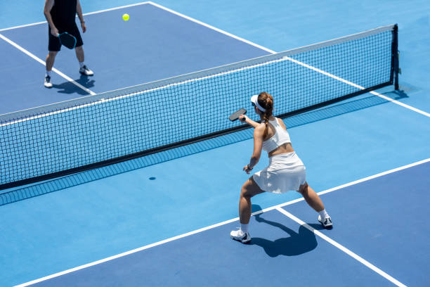 A female pickleball player returns a volley at the net on a dedicated pickleball court stock photo
