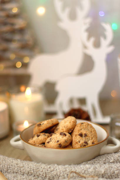 Various Christmas decorations, lit candles, cup of tea or coffee, cookies, books, presents and soft blanket on the table. Holiday hygge at home. Selective focus.