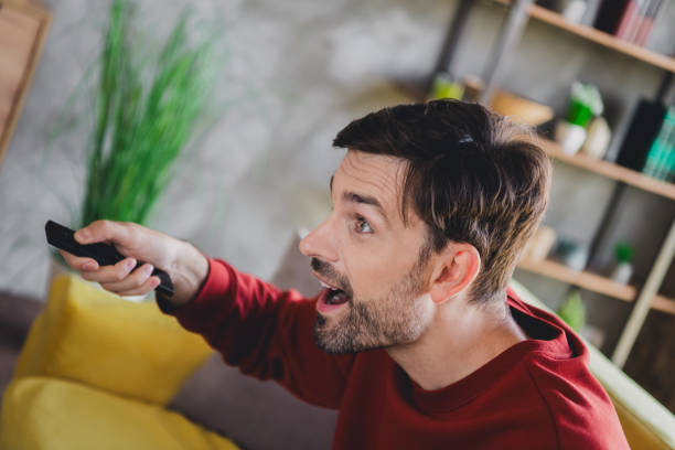 istock Young man in casual pullover enjoying a relaxed day indoors, using remote control at home, vibrant modern living room setting 2184518812