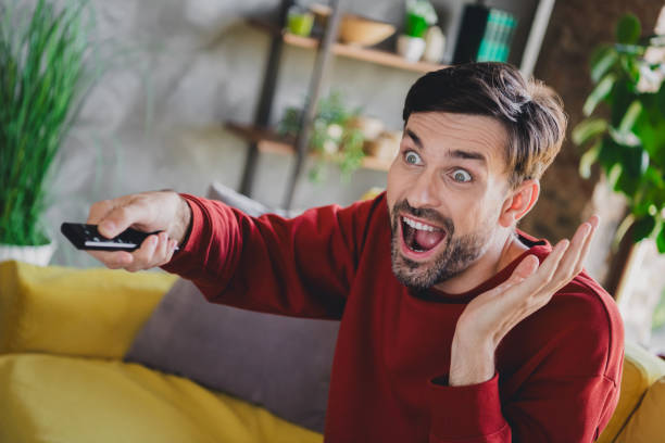 istock Young man in casual pullover excitedly watching TV at home during a relaxing day indoors 2184518835