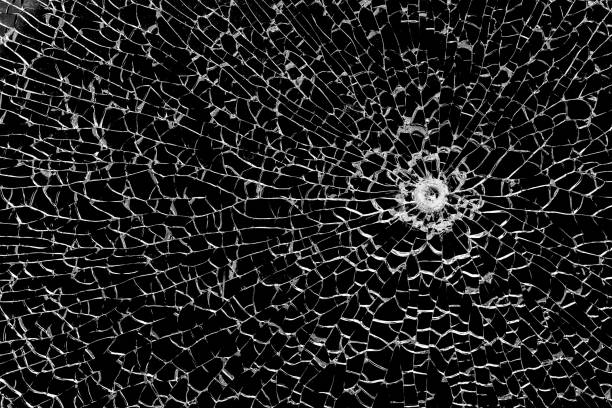 istock Texture of broken tempered glass with a bullet hole and diverging cracks on a black background. Design element. 2184521350