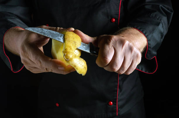 istock A chef in a black uniform uses a sharp knife to expertly peel a potato. The focused activity takes place in a dimly lit kitchen, showcasing culinary skill 2184524256