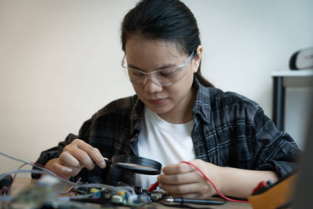 istock A woman is looking at a small electronic device with a magnifying glass. She is focused on the device and she is working on it 2184524416