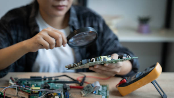 istock A woman is looking at a small electronic device with a magnifying glass. She is examining the device to see if it is working properly 2184524462