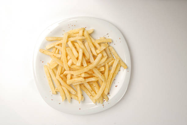 Stock photo showing close-up view of a meal of chicken cheeseburger in a white, sesame seed bread burger bun on a white plate served with crunchy French fry chips and a ramekin of tomato ketchup.