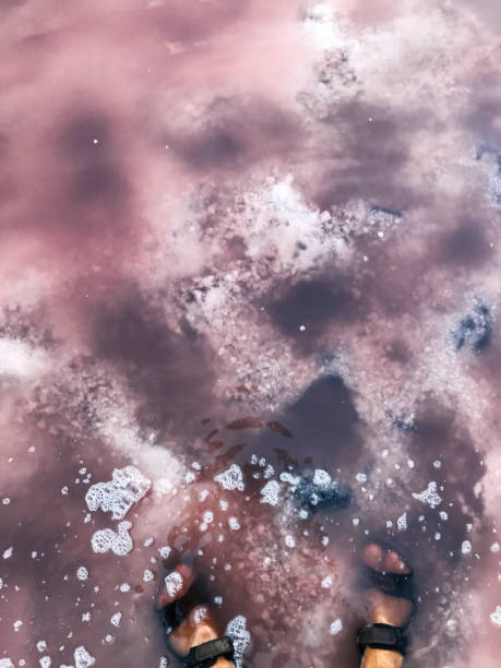 istock Feet in pink saltwater lake with foam and clouds reflection 2184525138