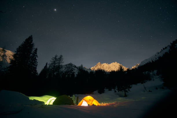 istock Night camping under a starry sky with tents illuminated by moonlight in a snowy mountain landscape 2184526976