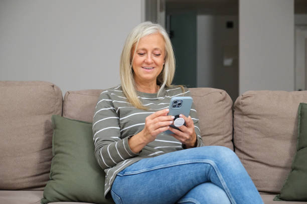 istock Smiling senior woman using smartphone on sofa at home 2184533116